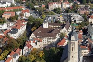 Eine Luftaufnahme des Hauptgebäudes der FSU Jena. Das altehrwürdige Gebäude steht im Stadtzentrum - davor ist der Glockenturm der Stadtkirche zu sehen.