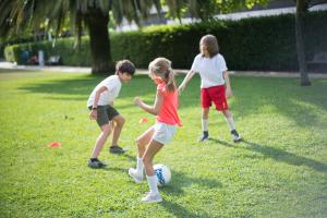 Grüne Wiese darauf 3 Kinder, 2 Jungen ein Mädchen spielen Fußball