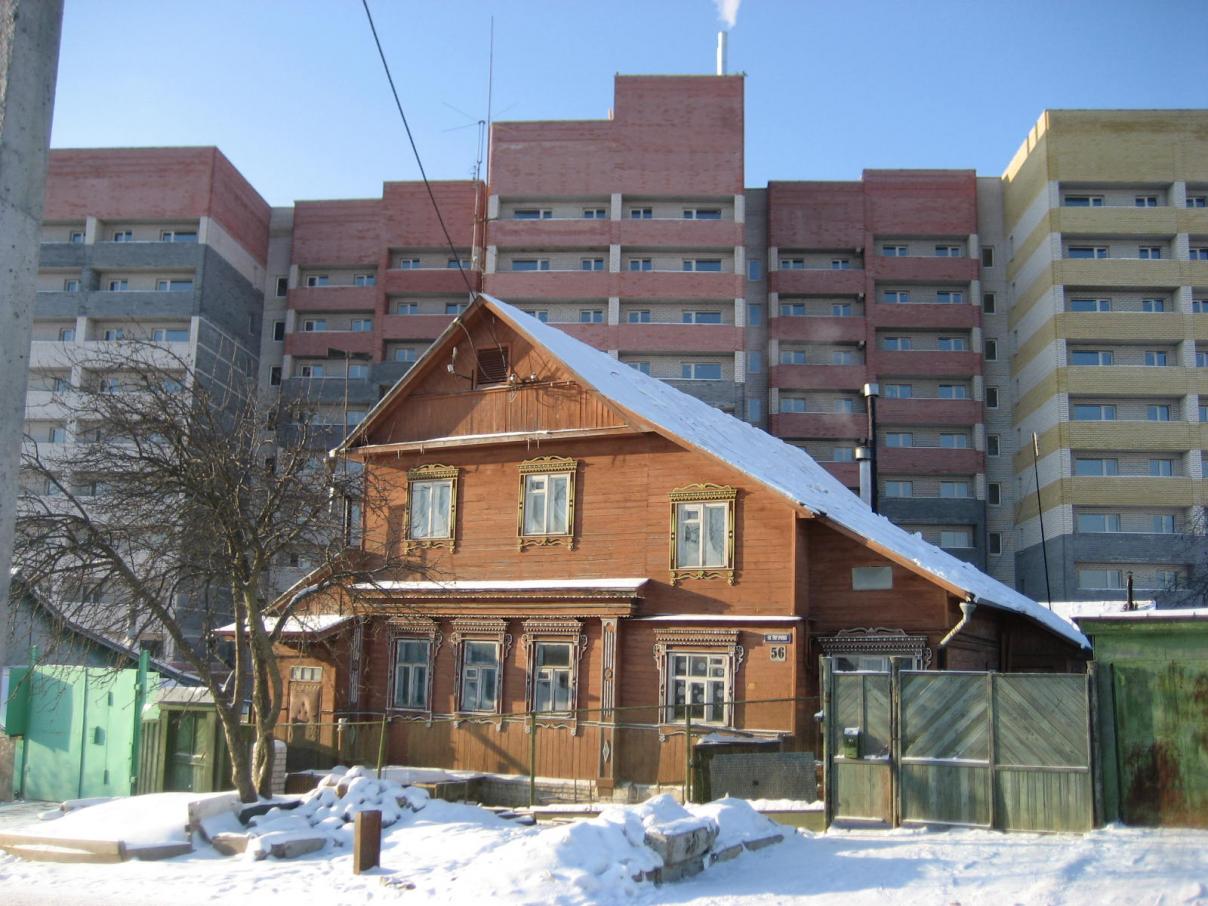 Alt und Neu liegen in Wladimir sehr nahe beieinander. Im Vordergrund ein traditionelles Holzhaus mit schön verzierten Fensterrahmen und dahinter bunte Wohnblocks, die in den winterlichen Himmel über Wladimir ragen