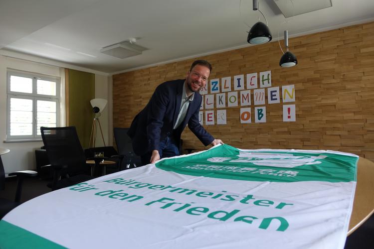 OB Dr. Thomas Nitzsche in seinem Büro mit der grün-weißen Flagge des Mayors for Peace Bündnisses