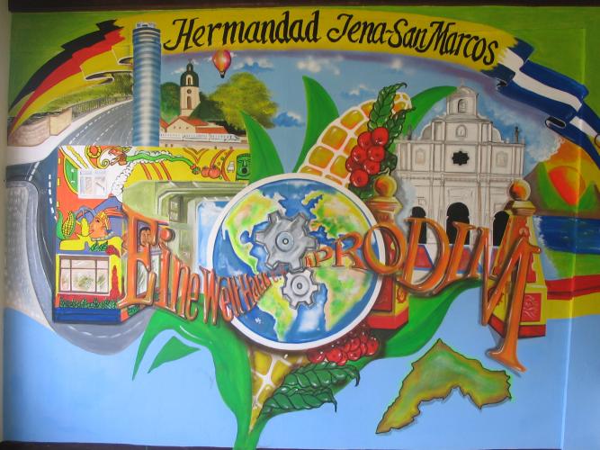 Ein farbenfrohes Wandbild schmückt das Büro des Partnerschaftsvereins APRODIM in San Marcos. Der Künstler heißt Javier Sanchez. Zu sehen ist mittig eine Weltkugel und rechts und links daneben typische Symbole der Partnerstädte Jena und San Marcos, darunter die Fassades des Eine-Welt-Haus e. V. 