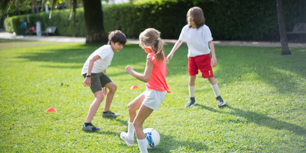 Grüne Wiese darauf 3 Kinder, 2 Jungen ein Mädchen spielen Fußball