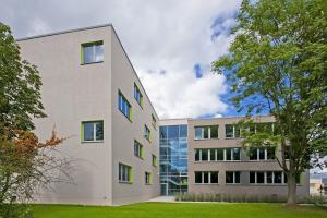 Das Staatliche Berufsbildende Schulzentrum Jena-Göschwitz mit grau-gläserner Fassade und in grüner Umgebung