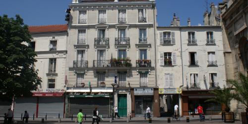 Eine Häuserfront im französischen Aubervilliers. Im Erdgeschoss sieht man verschiedene Läden, datunter eine Brasserie oder einen Tabakladen, die aber allesamt geschlossen sind